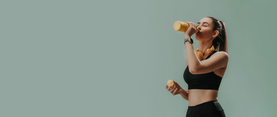 Jonge sportieve vrouw in sportkleding met draadloze hoofdtelefoon drinken uit fles over groene achtergrond, kopieer ruimte