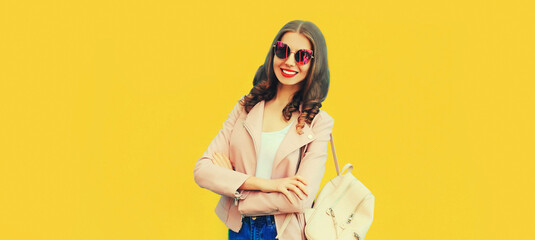 Portrait of beautiful smiling young woman wearing backpack on yellow background, blank copy space for advertising text