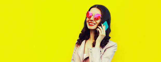 Portrait of happy smiling young woman calling on smartphone on yellow background, blank copy space for advertising text