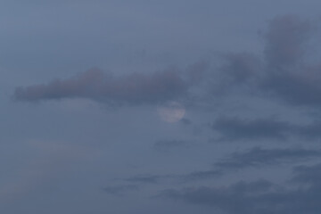 Obraz na płótnie Canvas Full moon rises behind clouds at dusk, lunar phase of natural satellite