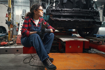 Woman auto mechanic sitting in car service garage