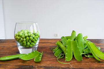 Green peas in glass bowl. fresh pea in the pod with green leaves. green peas on a brown wodden table