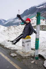 Asian woman sits happily on a pillar showing distance on the street in Sonamarg district. The travel destination in the winter.