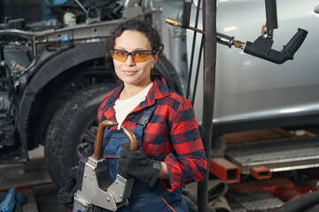 Female auto mechanic using car repair equipment in garage