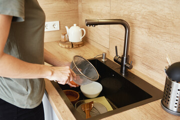 Woman washing dirty dishes in kitchen sink, Household and home hygiene routine.
