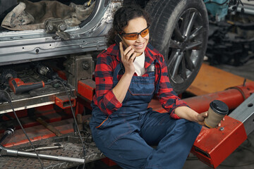 Happy woman car mechanic talking on mobile phone in garage