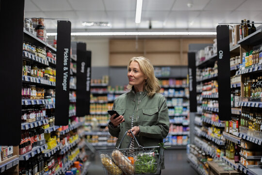 Mid adult female with smartphone in a grocery store 