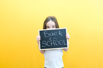 schoolgirl holding a tablet in her hands with the inscription Back to school on a yellow background.