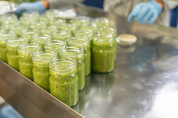 Pesto sauce Industrial process. High quality sauce production. Green pesto sauce in open jars on a...