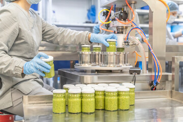 Pesto sauce with basil Industrial process. Factory worker working on vacuum sealing machine for canned food. production of Pesto sauce. Vacuum Seamer for Cylindrical Cans of Rotary Type