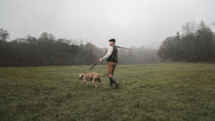 Hunter man with dog in traditional shooting clothes on field holding shotgun.