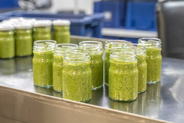 Pesto sauce Industrial process. High quality sauce production. Green pesto sauce in open jars on a...