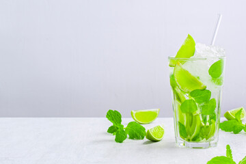 Fresh non-alcoholic mojito with crushed ice and straw in glass on white table. Delicious beverage made of fresh citrus fruit and slices of lime and mint closeup with copy space