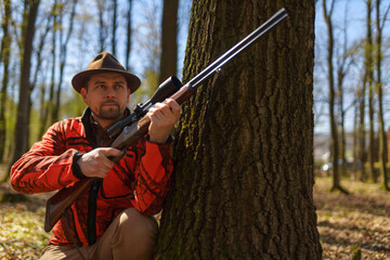 Fototapeta premium Hunter man with rifle gun waiting for prey in forest.