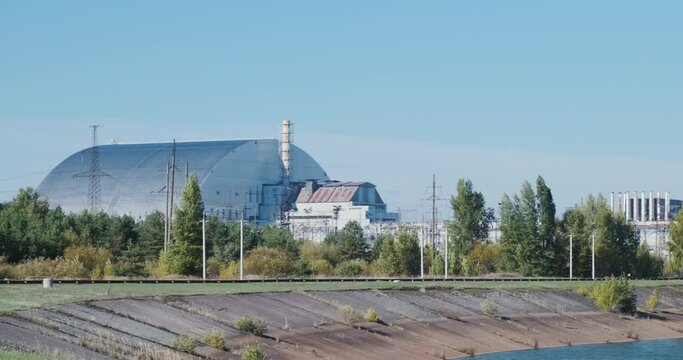 Radiation protection, a sarcophagus in Chernobyl, a reactor at a closed nuclear power plant, pipes and power lines. Panorama, daytime, clear sky.