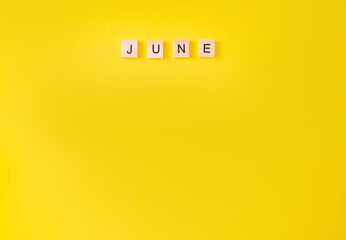 the word is June, written in wooden letters. June text on a yellow background for your design, top view concept. place for text