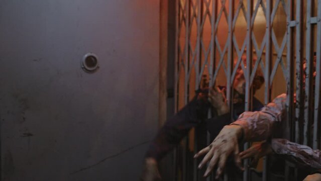 Locked-down of military woman with shaved head standing in dark creepy building, looking at three zombies stuck behind metal gate of old elevator reaching hands out