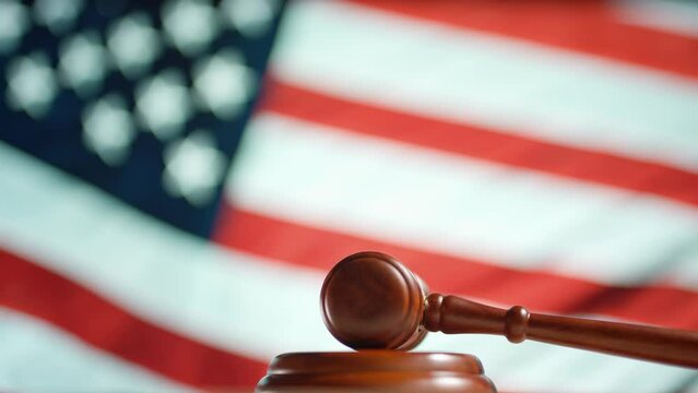 A judge gavel with a flag of United States of America on background. Close up of wooden hammer and legal lawyer books or codex. Sentence law or legal system and jurisprudence or court concept.