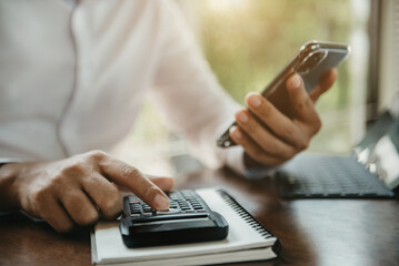 Male businessman hand using calculator and smartphone with calculate about cost at office.