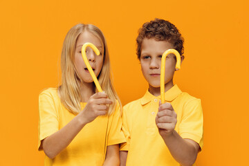 joyful children stand with yellow candies and look at them cheerfully. Horizontal photo on a yellow background with empty space for an advertising layout