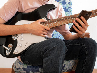 Young man learning to play the electric guitar through an app on his smartphone.