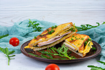 Roasted toast in scrambled eggs with ham, herbs and cheese cheddar. Delicious grilled breakfast sandwich