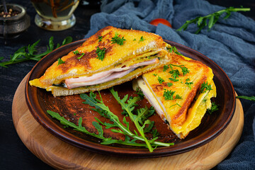 Roasted toast in scrambled eggs with ham, herbs and cheese cheddar. Delicious grilled breakfast sandwich