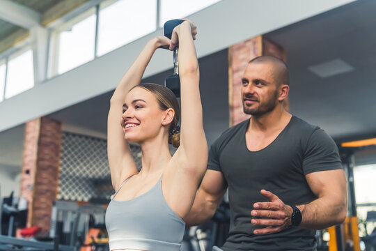 Caucasian personal trainer working with his client in gym, giving advices to a young fit woman lifting weights. Gym interior. High quality photo