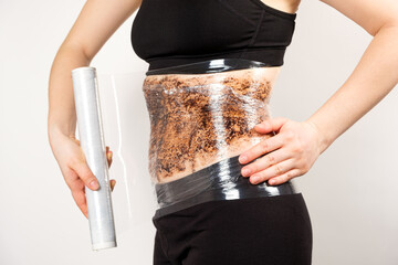 A woman makes a belly wrap with a coffee anti-cellulite body scrub. The concept of weight loss and...