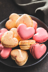 Heart shaped Sweet macarons on plate on black table.