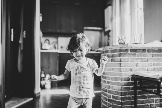 Funny toddler girl dancing indoors, little child play, baby having fun moving and jumping on the floor in a sunny white room at home or kindergarten. Black and white photo.