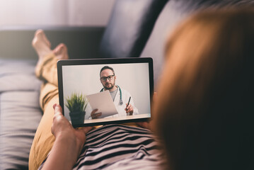 Woman lying on a sofa and talking with a doctor online using digital tablet. Telemedicine concept. - obrazy, fototapety, plakaty