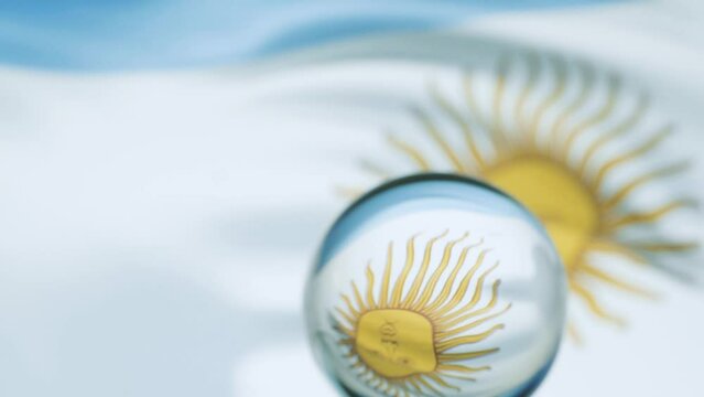 Argentinian flag is waving at a beautiful and peaceful sky in day while camera passes in front of a glass ball with dolly shot.
