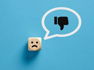 Unhappy face on a wooden cube with a dislike thumb down gesture icon in a speech bubble.