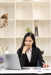 Asian businesswoman paying bills online with laptop in office Beautiful girl and checkbook phone willing to pay bills to start a business, financial calculator, accounting concept, vertical image.