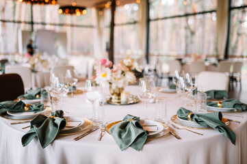 Festive banquet. Round tables which are beautifully decorated with plates, candles and a beautiful composition of flowers and table number in the center