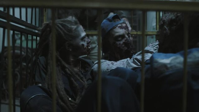 Military woman with shaved head moving away zombies in cage on wheels in dark basement of industrial building