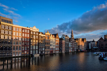 Fototapeta na wymiar Houses and tourist boats on Amsterdam canal pier Damrak on sunset. Amsterdam, Netherlands