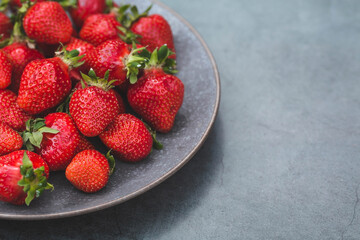Delicious, fresh strawberries in a stylish plate on a concrete background. Top view with space to copy.