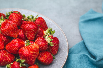 Delicious, fresh strawberries in a stylish plate on a concrete background. Top view with space to copy.