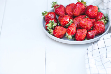 Delicious, fresh strawberries in a stylish plate on a white wooden background. Top view with space to copy.