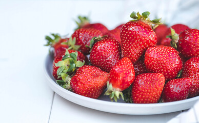 Delicious, fresh strawberries in a stylish plate on a white wooden background. Top view with space to copy.