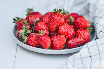 Delicious, fresh strawberries in a stylish plate on a white wooden background. Top view with space to copy.