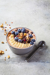 Chocolate banana smoothie bowl with granola, berries and hemp seeds, gray background. Healthy vegan recipe concept.