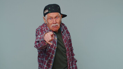 Hey you. Senior man 80s in shirt smiling excitedly and pointing to camera, choosing lucky lottery winner, indicating to awesome you. Elderly grandfather isolated alone on gray studio wall background