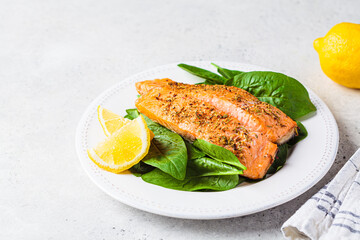 Fried with spices pieces of salmon with spinach on white plate. Diet recipe concept.