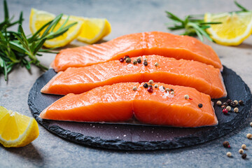 Pieces of raw salmon with spices and herbs on slate board, dark background.