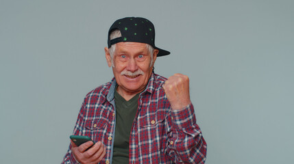 Happy excited one senior old man in casual shirt use mobile cell phone typing browsing shouting say wow yes found out great big win, good news, lottery goal achievemen, celebrating success, winning