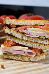 sandwich made of toast, tomato, cheese, ham, lettuce and mustard on wooden surface