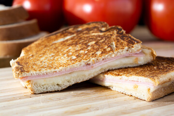 sandwich made of toast, tomato, cheese, ham, lettuce and mustard on wooden surface
